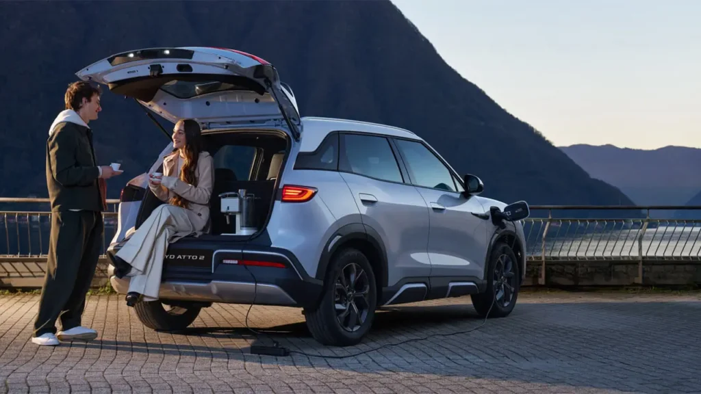 "Chinese cars for modern lifestyles: electric SUV BYD Atto 3 powering outdoor coffee setup by the lake with a couple enjoying nature."