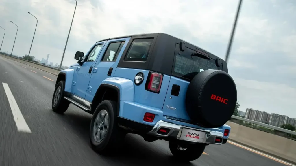 Blue BAIC BJ40 Plus driving on a highway, rear view with spare tire and BAIC branding.