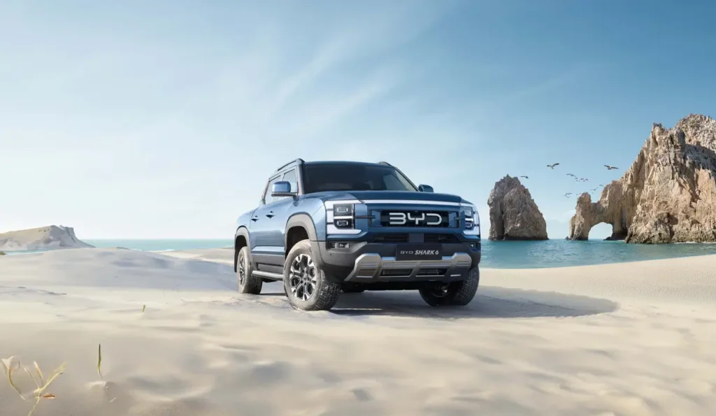 Review of BYD SHARK 6 — Hybrid Pickup from China | AutoChina BYD SHARK 6 electric pickup truck on a sandy beach with rock formations in the background